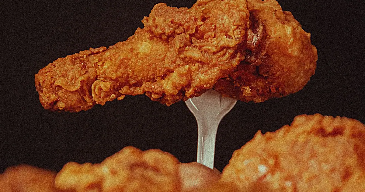 A crispy fried chicken drumstick held up on a fork - Dry rub vs sauced wings at Wingstop