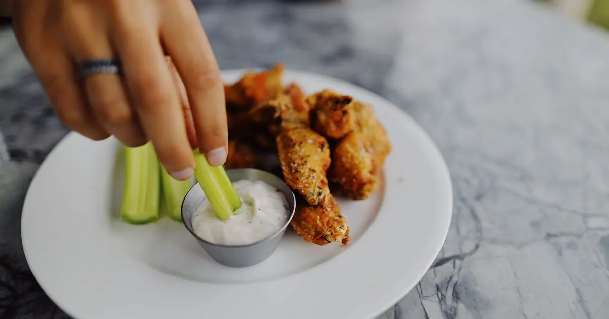 Celery sticks being dipped into ranch next to chicken wings - Low-calorie Wingstop: what to order and what to skip