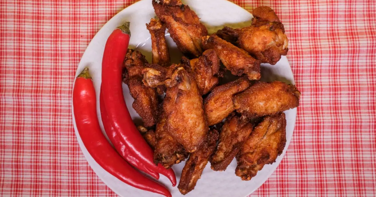 Fried chicken wings on a plate with red chili peppers - Spicy Wingstop flavors, ranked from mild to Atomic